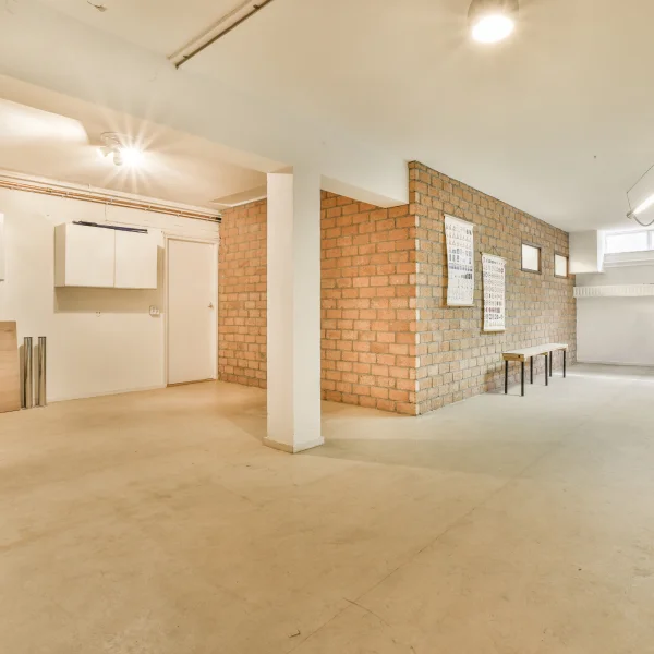 Grande salle vide avec un mur en briques et un banc, typique d'un espace commercial.