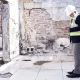 Un homme en casque et gilet se tient dans un vieux bâtiment, observant l'environnement autour de lui.
