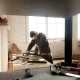 Un homme utilise une scie sur table dans une pièce, illustrant les étapes d'une rénovation réussie.