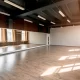 Studio de danse vide avec un grand miroir et un sol en bois, situé dans un espace commercial.