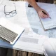 Une personne travaille sur un ordinateur portable tout en portant un casque de sécurité sur un chantier de construction.