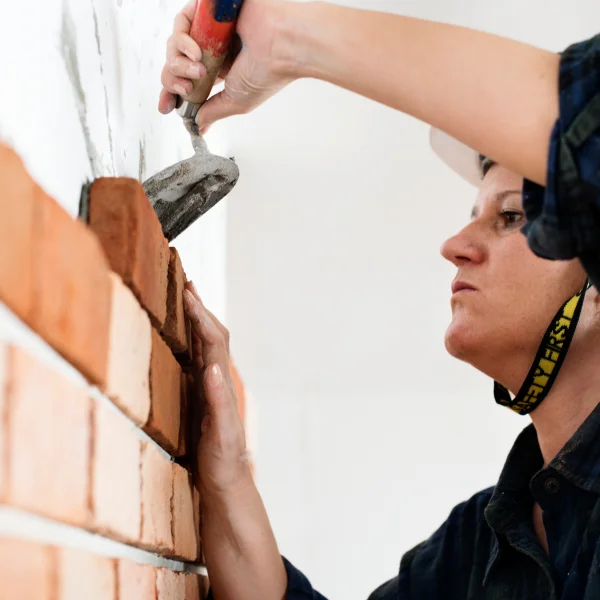  Une femme utilise un marteau pour construire un mur en briques avec des matériaux de construction.