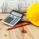 Un casque de sécurité, une calculatrice et un crayon posés sur une table, symbolisant l'estimation des coûts.